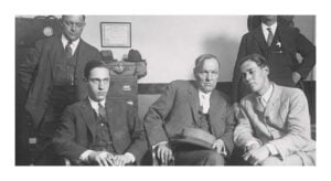Black and white photo of several men sitting in a row.