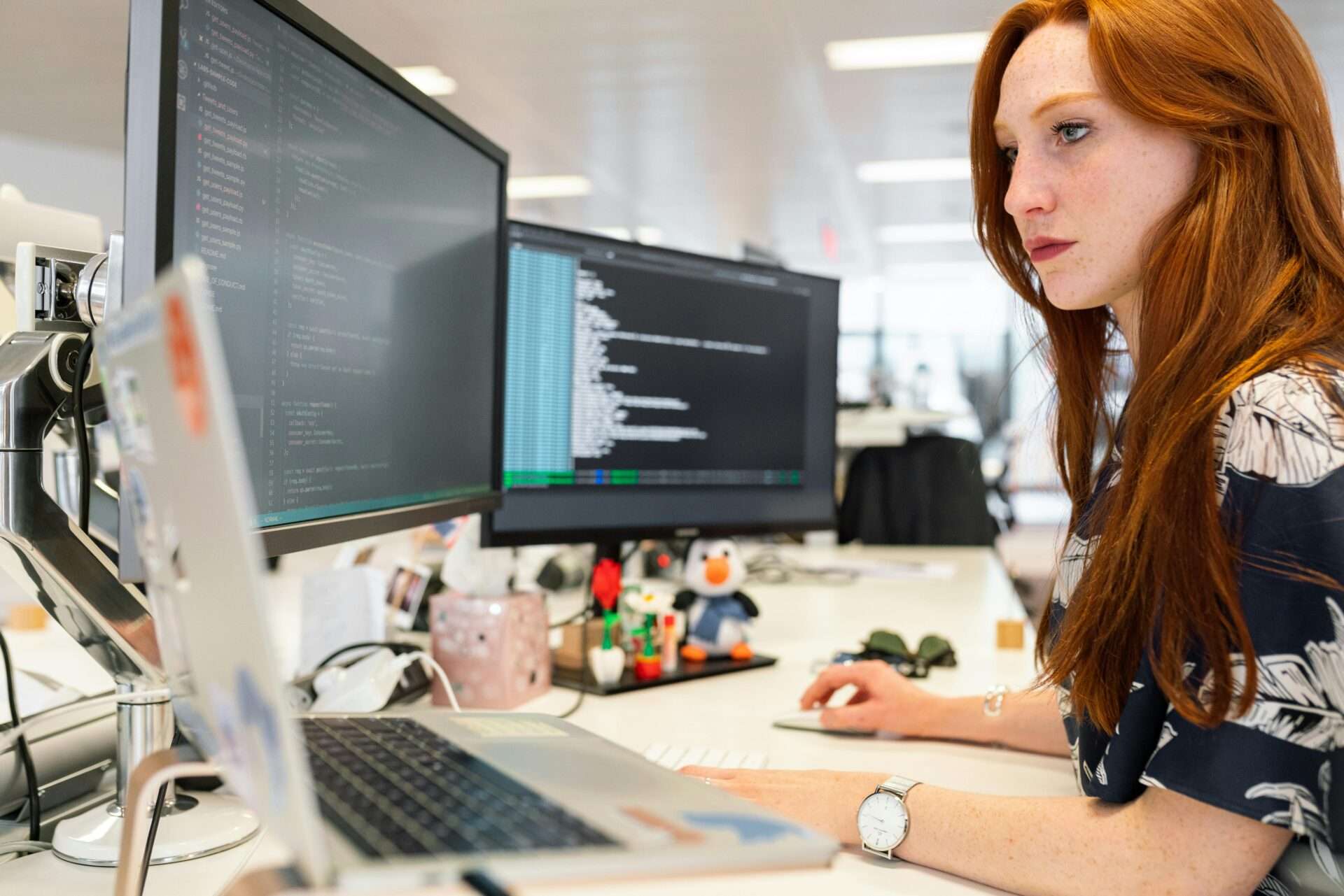 Woman sitting at a desk enhancing productivity by using three computer screens.
